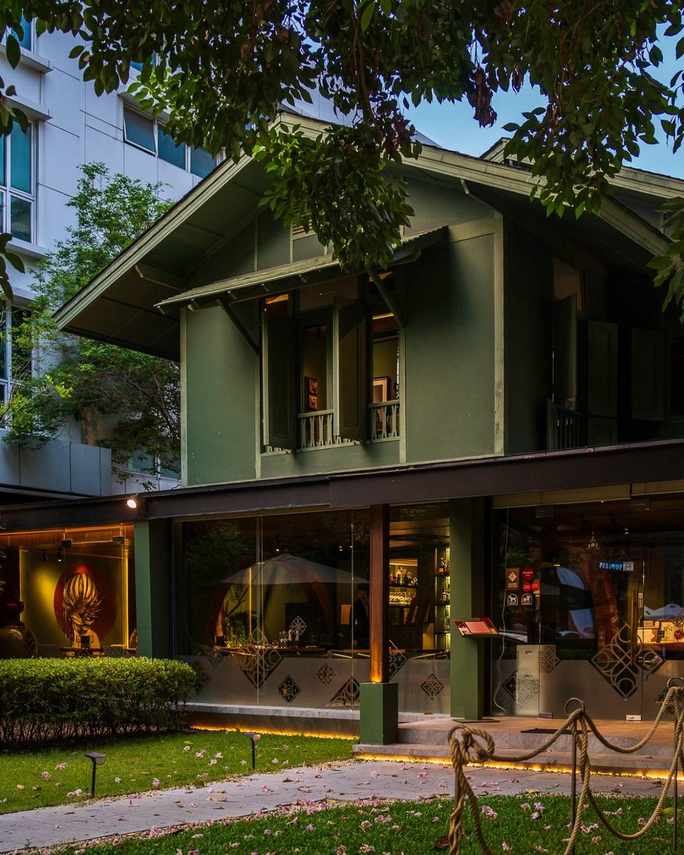 North's green two-storey house at dusk under the trees, lit from inside, the garden path in front